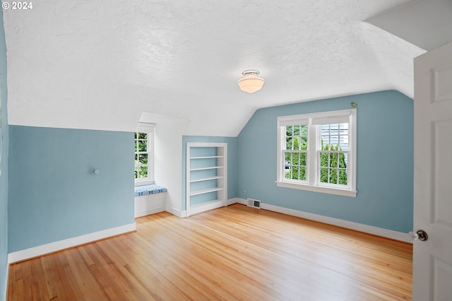 additional living space with wood-type flooring, built in features, a textured ceiling, and vaulted ceiling