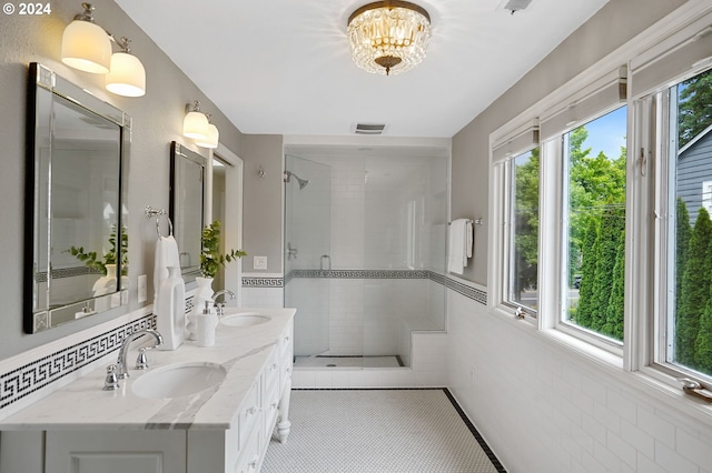 bathroom featuring a notable chandelier, vanity, a shower with shower door, and tile walls