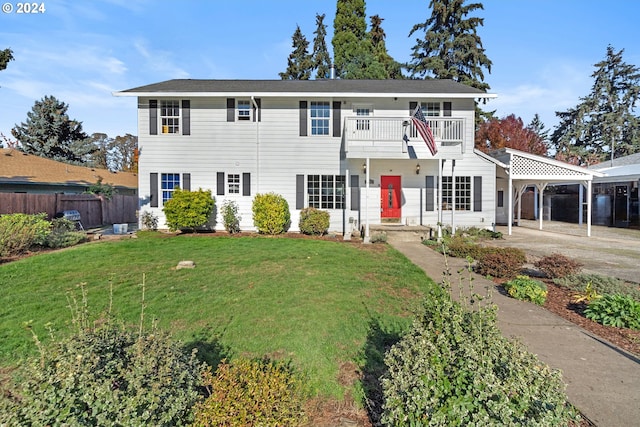 colonial home with a balcony, concrete driveway, a carport, fence, and a front yard