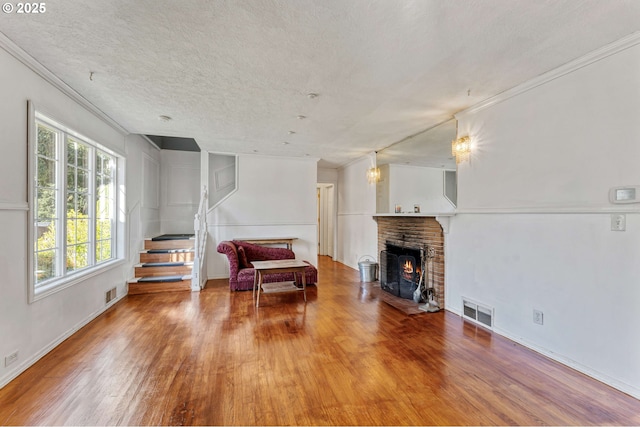 living area featuring a textured ceiling, wood finished floors, visible vents, and crown molding