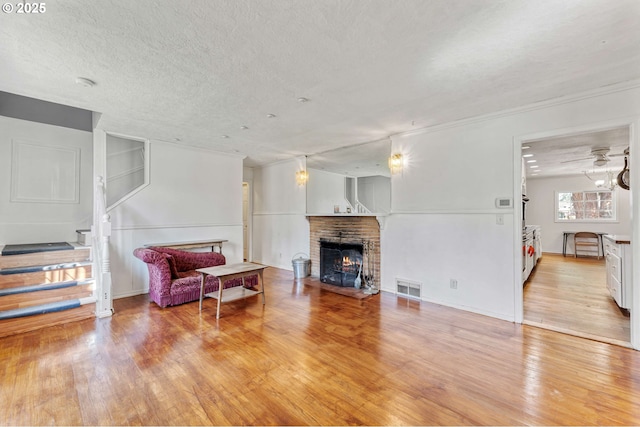 living room featuring light wood finished floors, a textured ceiling, visible vents, a brick fireplace, and stairs