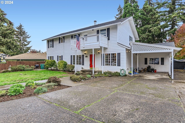 colonial inspired home featuring a balcony, concrete driveway, fence, an attached carport, and a front yard