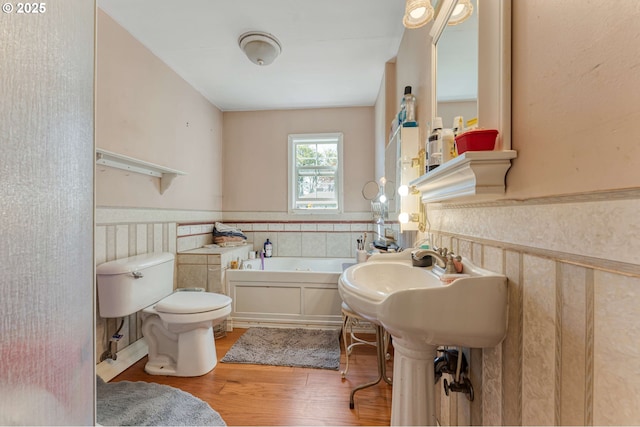 bathroom featuring a bath, a wainscoted wall, wood finished floors, and toilet
