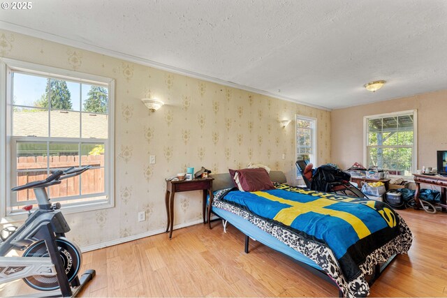 bedroom with wallpapered walls, wood finished floors, a textured ceiling, and ornamental molding