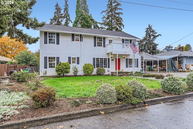colonial home with a balcony, a front lawn, and fence
