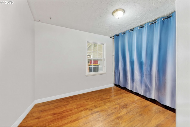 empty room featuring baseboards, wood finished floors, and a textured ceiling