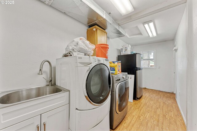 laundry room featuring light wood-type flooring, separate washer and dryer, a sink, and cabinet space