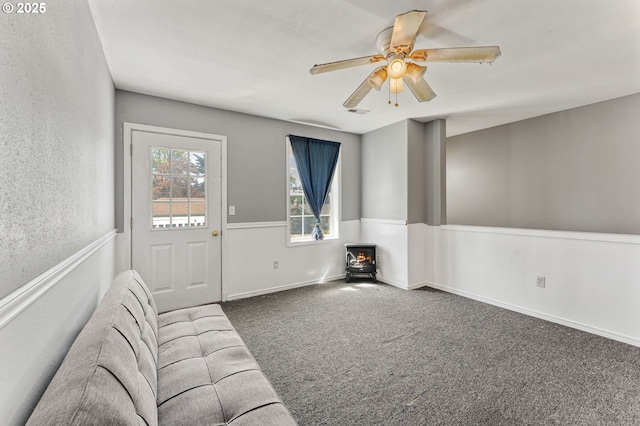 unfurnished living room with ceiling fan, carpet flooring, and a wood stove