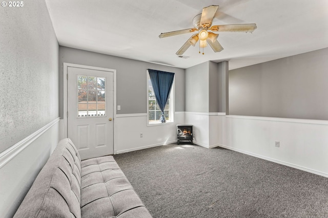 unfurnished living room with a wood stove, carpet flooring, ceiling fan, and visible vents