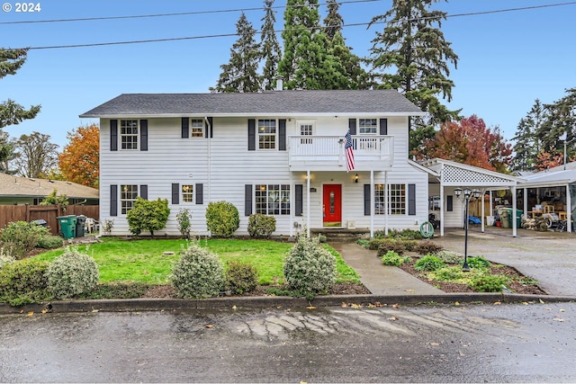 colonial house with roof with shingles, a front lawn, concrete driveway, fence, and a balcony