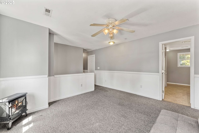 unfurnished living room with carpet floors, a ceiling fan, a wood stove, and visible vents