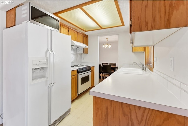 kitchen featuring pendant lighting, white appliances, sink, backsplash, and a notable chandelier