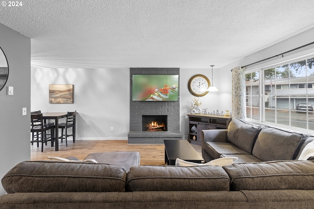 living room with hardwood / wood-style floors, a textured ceiling, and a brick fireplace