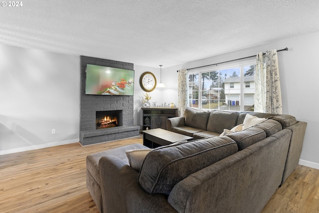 living room featuring light hardwood / wood-style flooring, a textured ceiling, and a brick fireplace