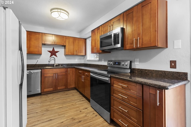 kitchen featuring dark stone countertops, sink, light hardwood / wood-style flooring, and appliances with stainless steel finishes