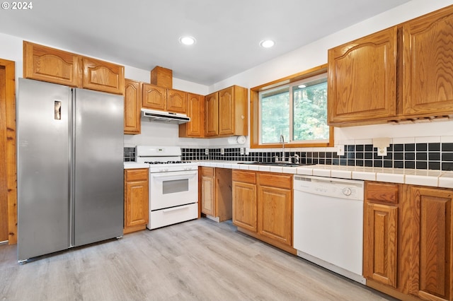 kitchen featuring tile countertops, sink, light hardwood / wood-style flooring, and white appliances