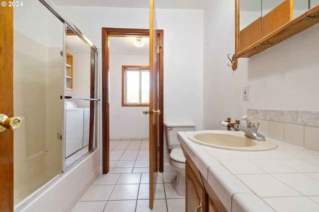 full bathroom with washer / clothes dryer, combined bath / shower with glass door, toilet, vanity, and tile patterned flooring