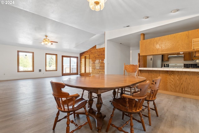 dining area with lofted ceiling, wooden walls, light hardwood / wood-style floors, and ceiling fan