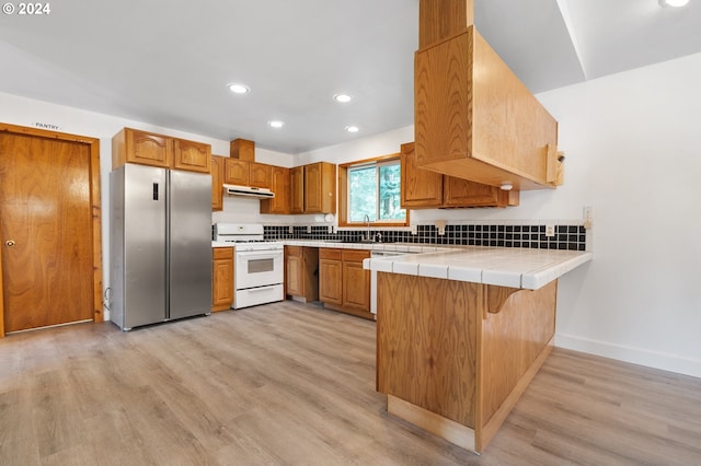 kitchen featuring kitchen peninsula, tile countertops, stainless steel refrigerator, light hardwood / wood-style flooring, and white range oven