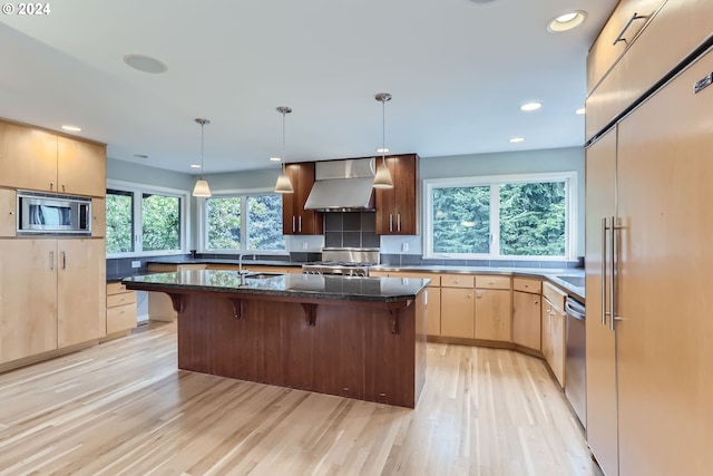 kitchen with built in appliances, wall chimney exhaust hood, a kitchen island, and a wealth of natural light