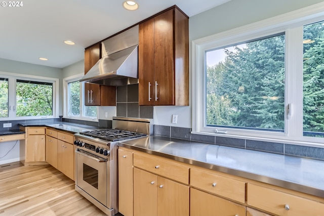 kitchen with high end stainless steel range, wall chimney exhaust hood, and light wood-type flooring