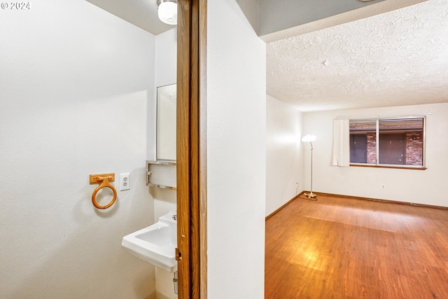 interior space with a textured ceiling, a sink, wood finished floors, and baseboards