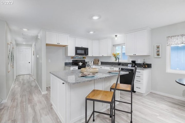 kitchen with black appliances, light stone countertops, a center island, white cabinetry, and a kitchen bar