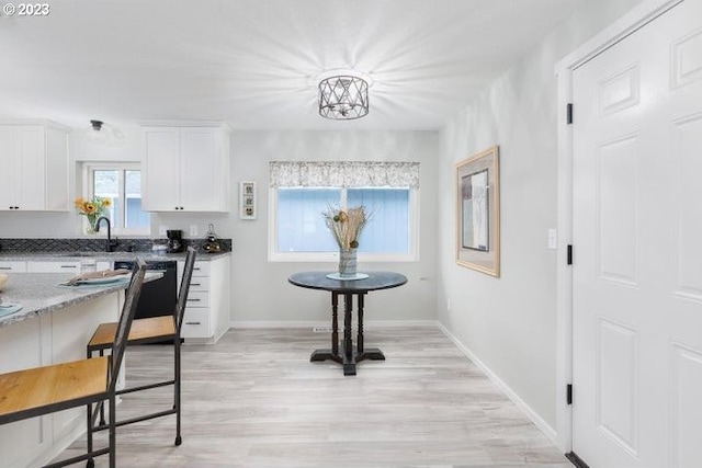 kitchen with white cabinets, sink, light hardwood / wood-style flooring, an inviting chandelier, and dark stone counters