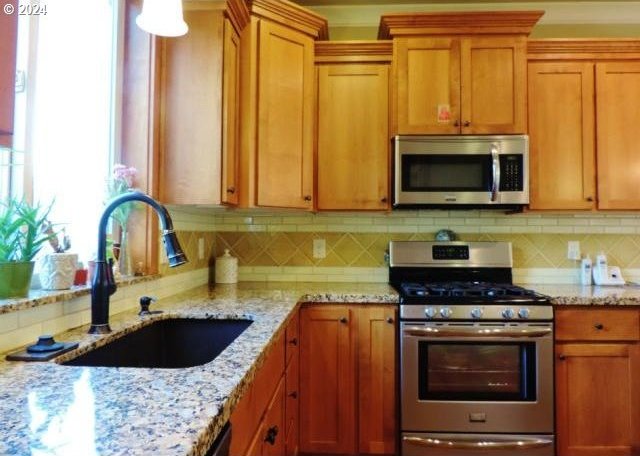 kitchen featuring backsplash, sink, stainless steel appliances, and light stone counters