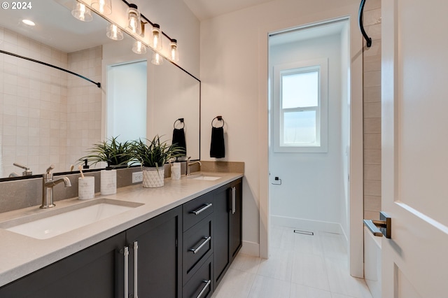 bathroom featuring double vanity, tiled shower, baseboards, and a sink