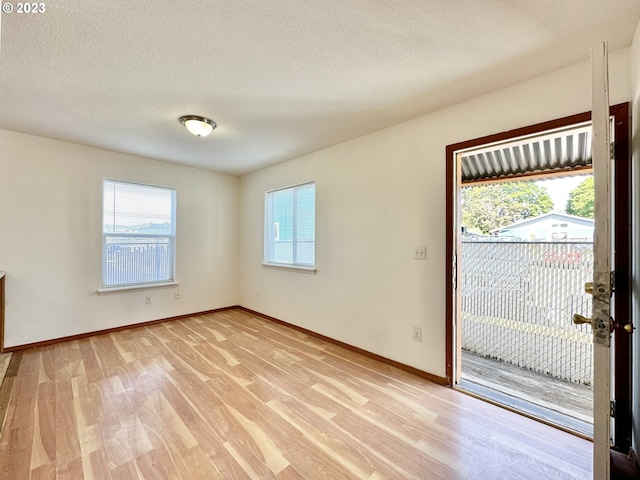 empty room featuring plenty of natural light, light wood-type flooring, and a textured ceiling