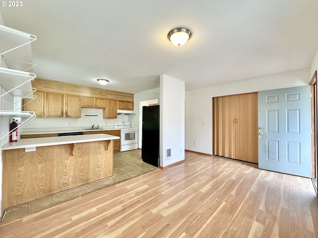 kitchen featuring kitchen peninsula, black fridge, light hardwood / wood-style floors, sink, and white range with electric cooktop