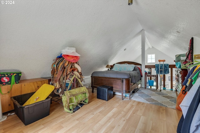 bedroom with wood-type flooring, vaulted ceiling, and a textured ceiling