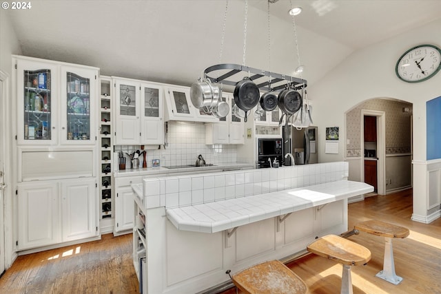 kitchen with tile countertops, vaulted ceiling, white cabinets, and a kitchen bar