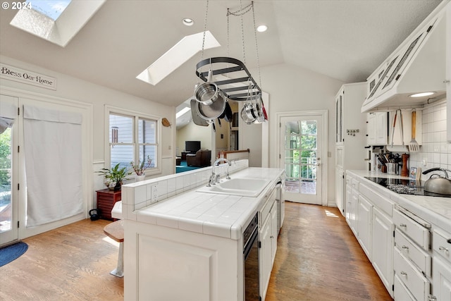 kitchen featuring sink, lofted ceiling with skylight, black electric stovetop, white cabinets, and tile countertops