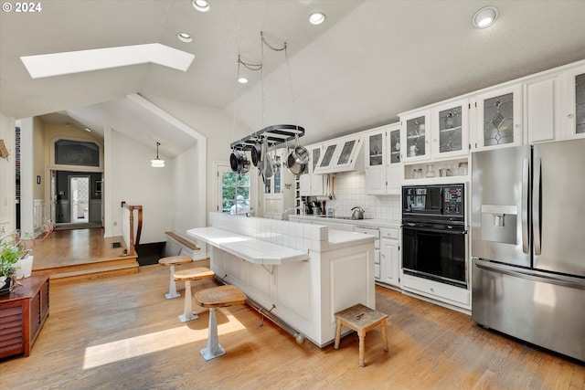 kitchen featuring vaulted ceiling with skylight, decorative light fixtures, black microwave, white cabinetry, and stainless steel fridge