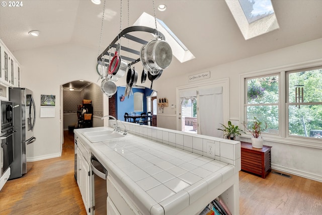 kitchen featuring sink, appliances with stainless steel finishes, white cabinetry, vaulted ceiling with skylight, and tile countertops