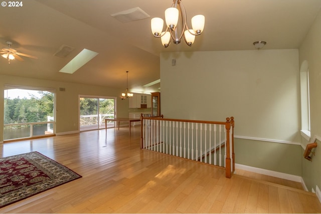 spare room with ceiling fan with notable chandelier, light hardwood / wood-style flooring, and vaulted ceiling