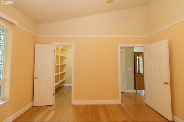 unfurnished bedroom featuring a walk in closet, a closet, light hardwood / wood-style floors, and lofted ceiling