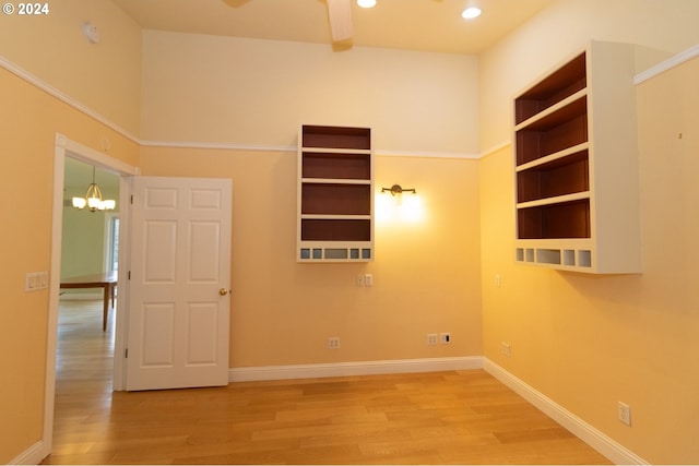 empty room with wood-type flooring and ceiling fan with notable chandelier