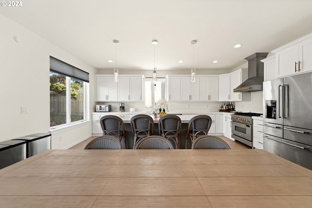 kitchen with a breakfast bar area, wall chimney exhaust hood, white cabinetry, high end appliances, and a kitchen island
