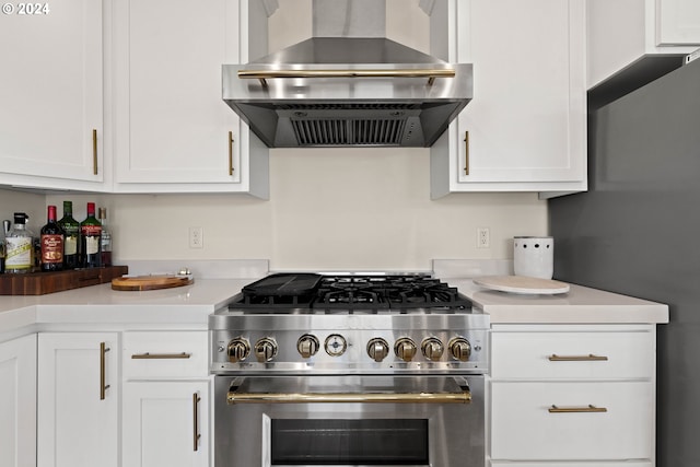 kitchen with light countertops, white cabinetry, stainless steel range, and wall chimney range hood
