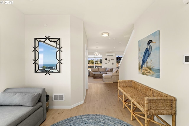 hall featuring baseboards, visible vents, light wood-style flooring, and a wall mounted AC
