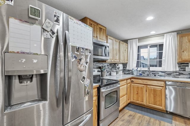 kitchen featuring sink, stainless steel appliances, tasteful backsplash, and light hardwood / wood-style flooring