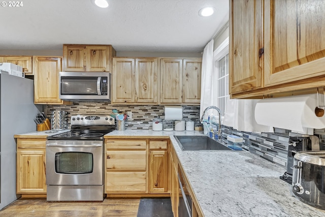 kitchen with sink, backsplash, light hardwood / wood-style floors, light brown cabinetry, and appliances with stainless steel finishes