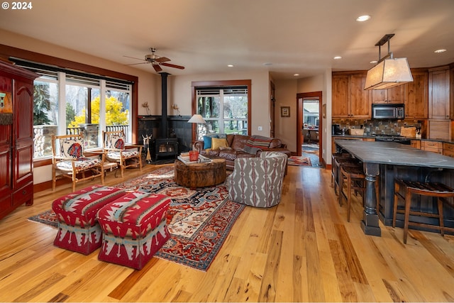 living room with ceiling fan, light hardwood / wood-style flooring, and a wood stove