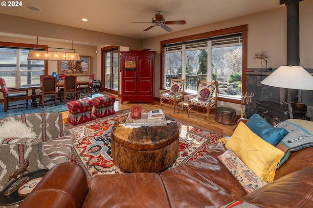 living room with a wealth of natural light, ceiling fan, a wood stove, and wood-type flooring