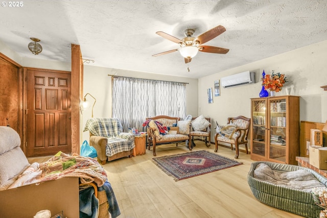 living room with a textured ceiling, light hardwood / wood-style flooring, a wall unit AC, and ceiling fan