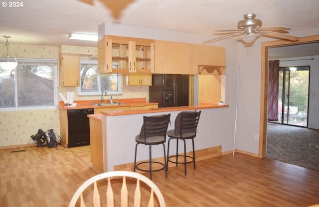 kitchen with light wood-type flooring, a breakfast bar, black appliances, and kitchen peninsula