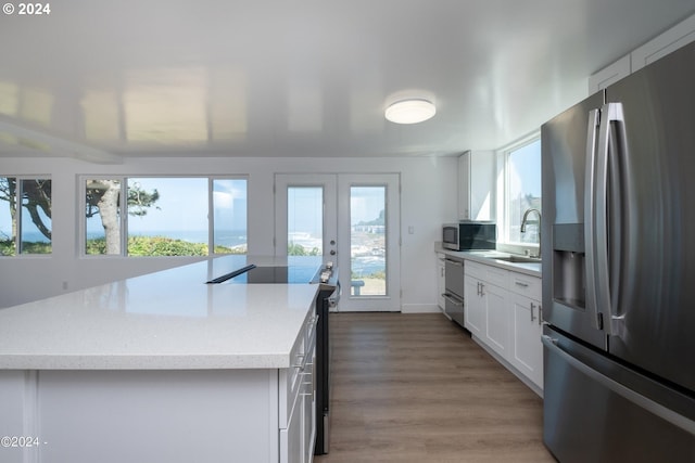 kitchen featuring wood-type flooring, stainless steel appliances, a center island, and white cabinetry